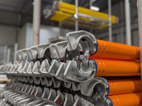 Stacked orange powder-coated scaffold braces with cast hook-style end fittings.